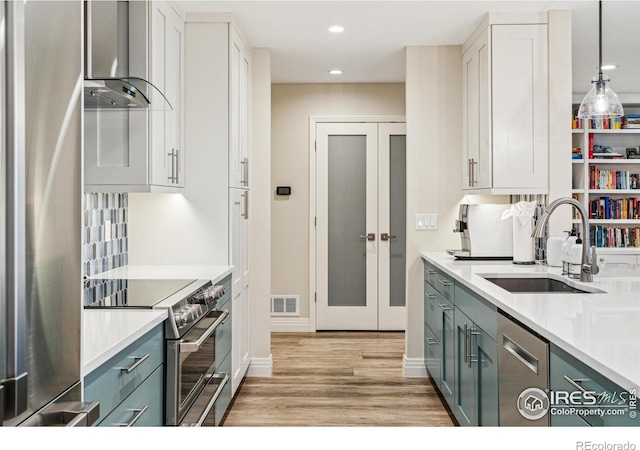 kitchen featuring stainless steel appliances, a sink, visible vents, light countertops, and wall chimney exhaust hood