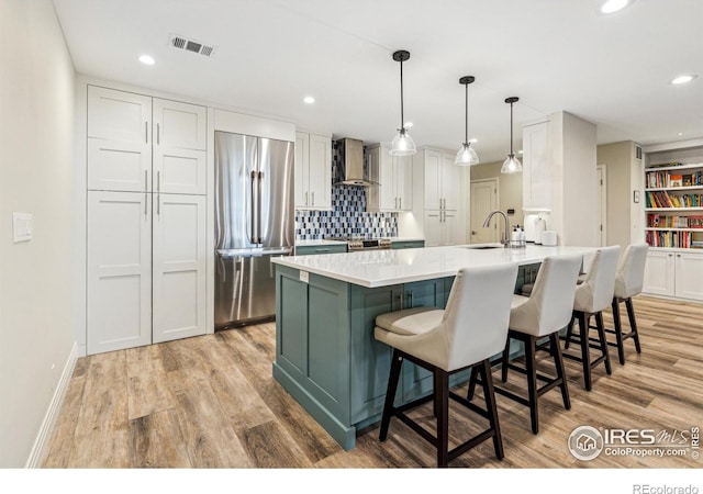 kitchen featuring a sink, visible vents, white cabinetry, stainless steel refrigerator, and wall chimney exhaust hood