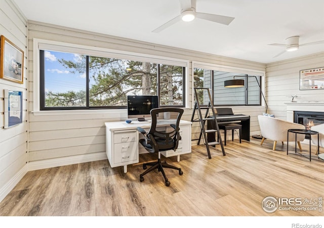 office area featuring ceiling fan, baseboards, wood finished floors, and a glass covered fireplace