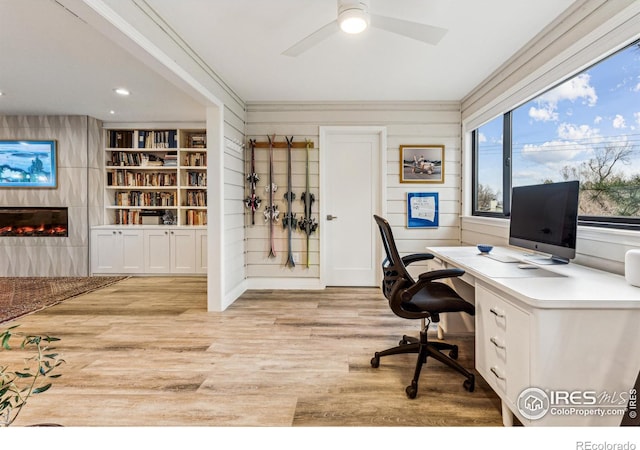 home office featuring a large fireplace, light wood-style flooring, ornamental molding, and ceiling fan