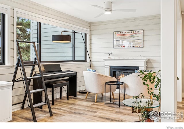 interior space featuring a warm lit fireplace, ceiling fan, wooden walls, and wood finished floors