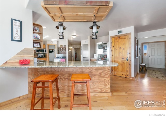 kitchen featuring stone counters, light wood-style flooring, a peninsula, stainless steel microwave, and decorative light fixtures