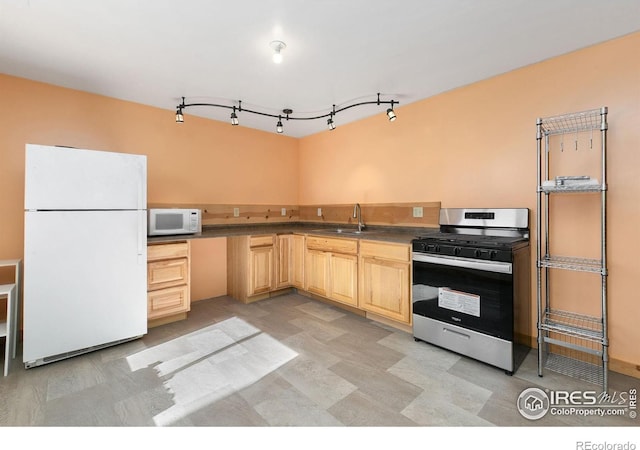 kitchen with light brown cabinetry, white appliances, dark countertops, and a sink