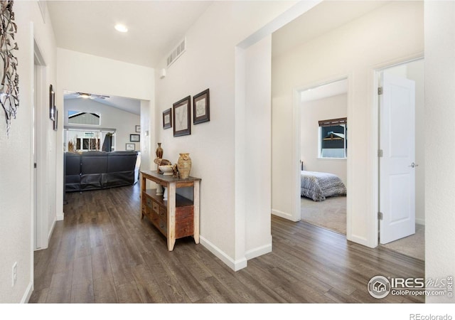 hallway featuring visible vents, vaulted ceiling, baseboards, and wood finished floors