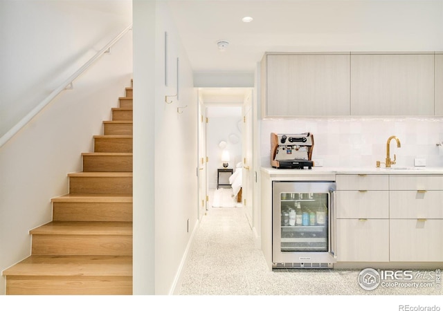 interior space featuring beverage cooler, a sink, stairs, and decorative backsplash