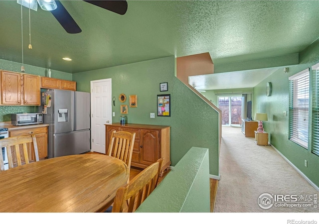 dining room with light colored carpet, a textured wall, ceiling fan, a textured ceiling, and baseboards