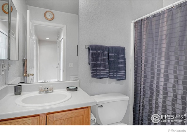 bathroom featuring toilet, a shower with curtain, vanity, and a textured wall