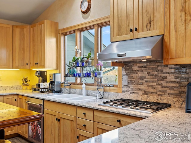 kitchen with lofted ceiling, under cabinet range hood, stainless steel gas cooktop, a sink, and tasteful backsplash