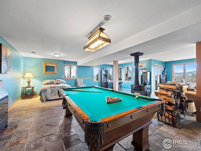 recreation room featuring a wood stove, a healthy amount of sunlight, a textured ceiling, and stone tile floors