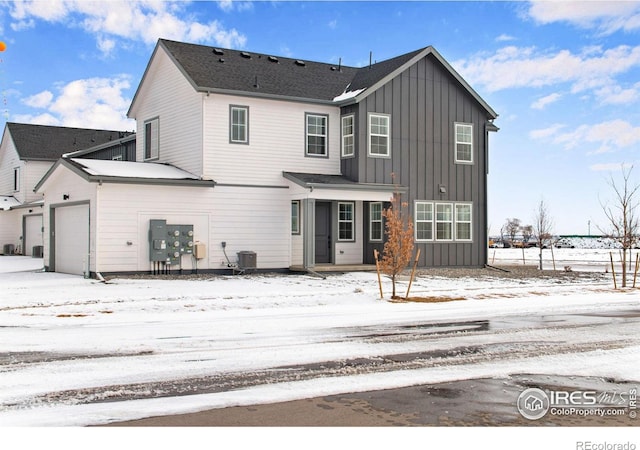 snow covered property with a garage, central AC unit, and board and batten siding