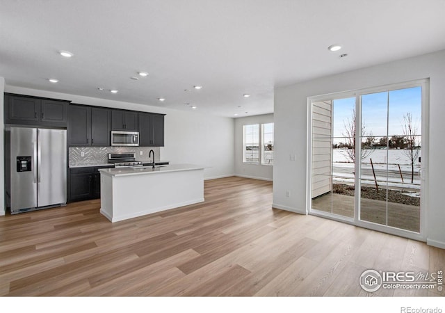 kitchen with dark cabinets, stainless steel appliances, light wood-style floors, light countertops, and decorative backsplash