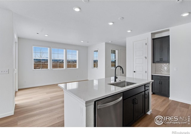 kitchen with light wood finished floors, dishwasher, an island with sink, backsplash, and a sink