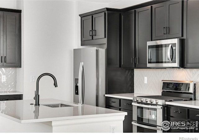 kitchen with tasteful backsplash, a kitchen island with sink, stainless steel appliances, dark cabinetry, and a sink