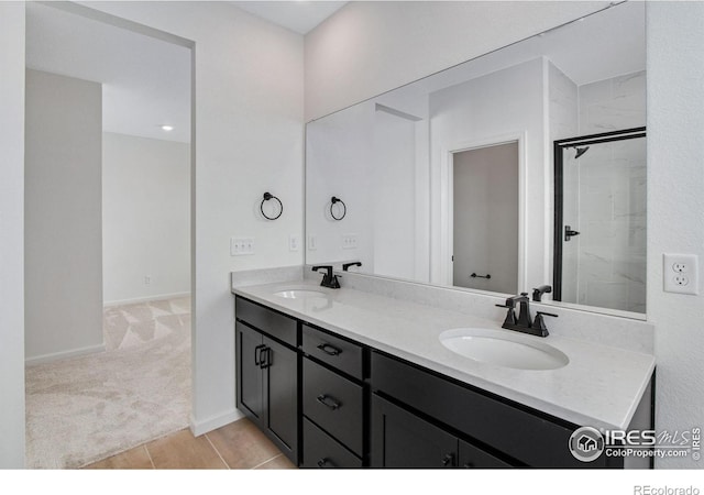 full bathroom with double vanity, a sink, a shower with shower door, and baseboards