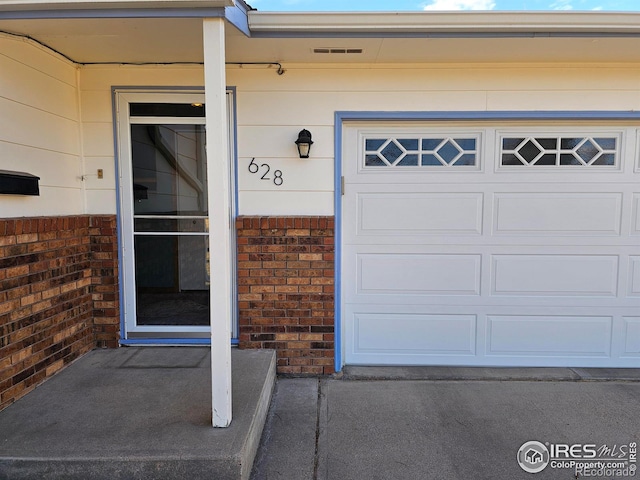 doorway to property with a garage and brick siding