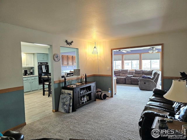 living room featuring a ceiling fan, light carpet, a textured ceiling, and baseboards