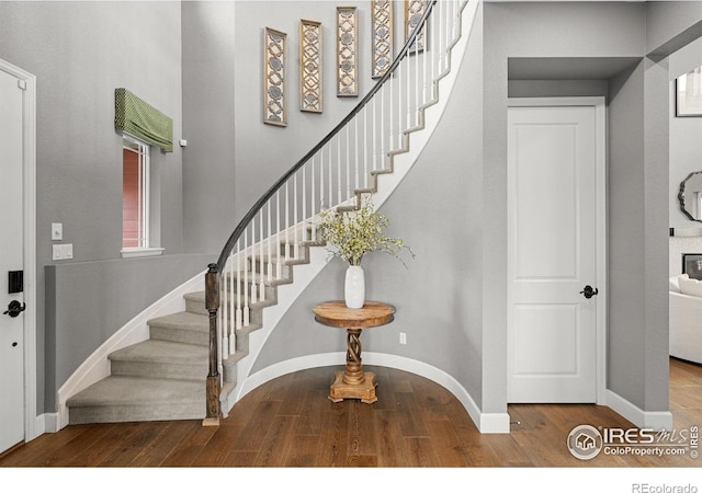 foyer entrance featuring a high ceiling, stairway, wood finished floors, and baseboards