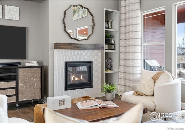 living room with built in shelves, a tiled fireplace, and wood finished floors