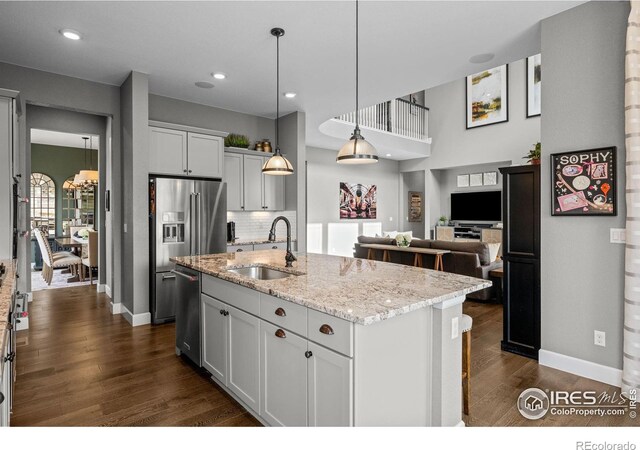 kitchen featuring a center island with sink, decorative backsplash, dark wood-style floors, appliances with stainless steel finishes, and a sink