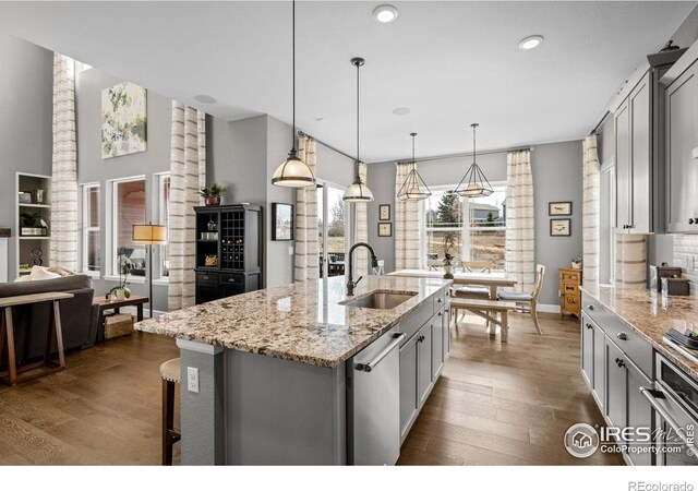 kitchen featuring a kitchen island with sink, a sink, gray cabinets, dishwasher, and dark wood finished floors