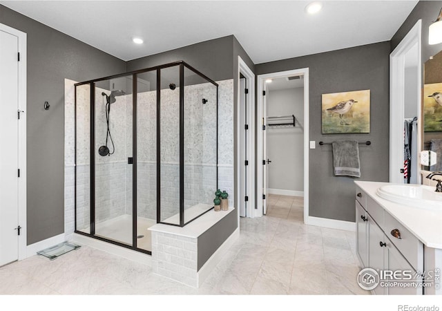 bathroom featuring a walk in closet, marble finish floor, a shower stall, vanity, and baseboards