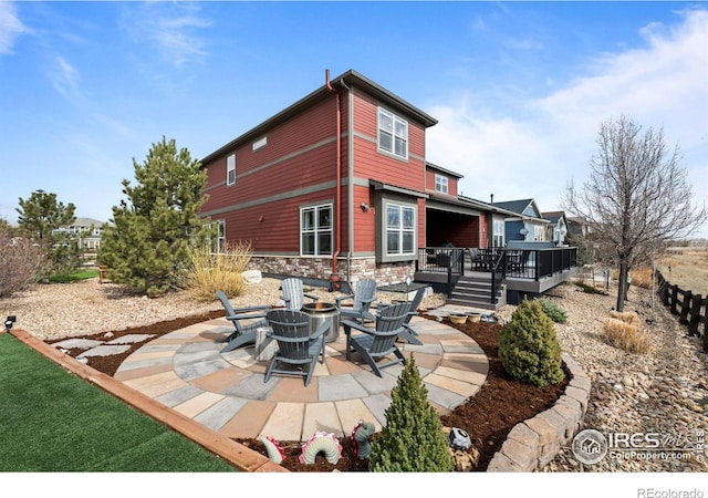 rear view of house featuring an outdoor fire pit, stone siding, a patio, and a wooden deck