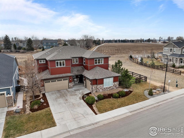 prairie-style house featuring stone siding, fence, concrete driveway, an attached garage, and a shingled roof