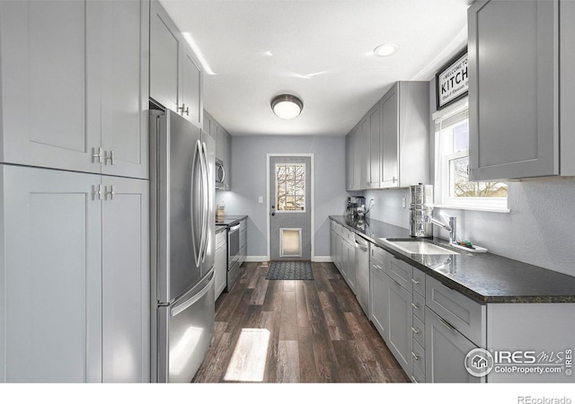 kitchen with dark countertops, dark wood-style floors, appliances with stainless steel finishes, gray cabinets, and a sink