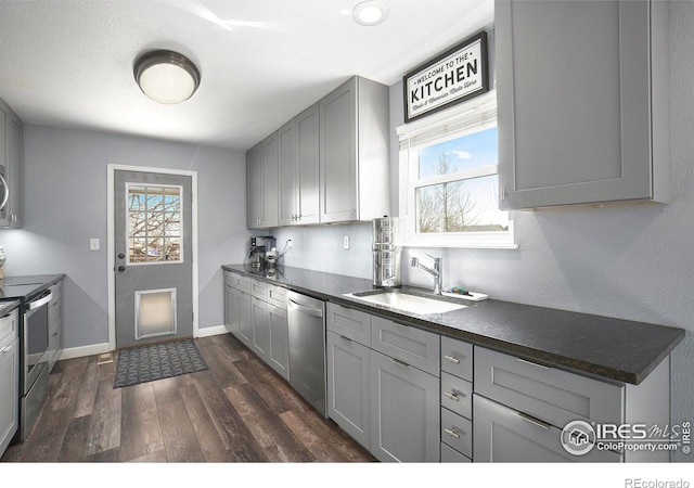 kitchen with a sink, stainless steel appliances, dark countertops, and gray cabinets