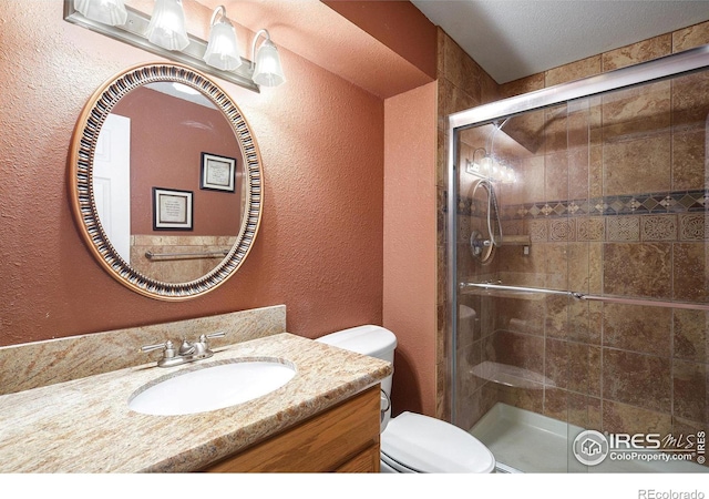 full bathroom with a textured wall, a shower stall, toilet, and vanity