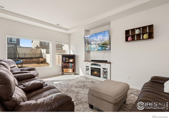 carpeted living room with visible vents, a lit fireplace, and baseboards