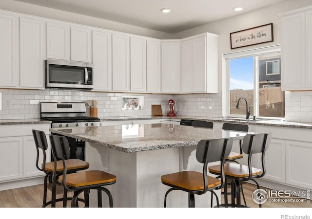 kitchen with white cabinets, decorative backsplash, stainless steel appliances, a kitchen bar, and a sink