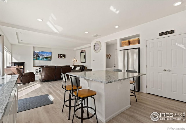 kitchen featuring light wood-style floors, a kitchen breakfast bar, a wealth of natural light, a center island, and freestanding refrigerator