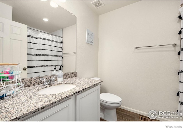 bathroom featuring toilet, wood finished floors, vanity, visible vents, and baseboards