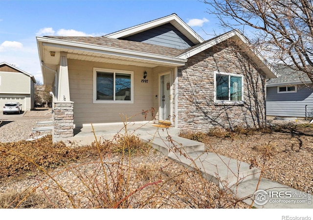 view of front facade with stone siding and roof with shingles