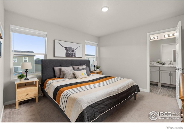 bedroom featuring light colored carpet, a sink, baseboards, and ensuite bathroom