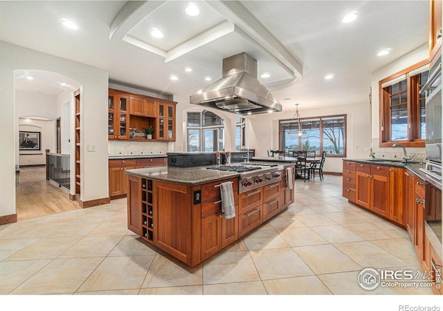 kitchen featuring island exhaust hood, open shelves, stainless steel gas stovetop, brown cabinetry, and a sink