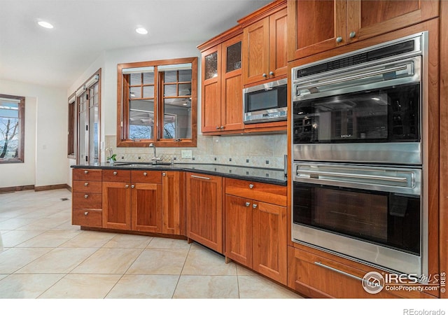 kitchen featuring appliances with stainless steel finishes, brown cabinetry, a sink, and tasteful backsplash