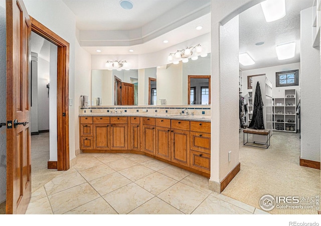 bathroom with double vanity, a sink, a walk in closet, and baseboards