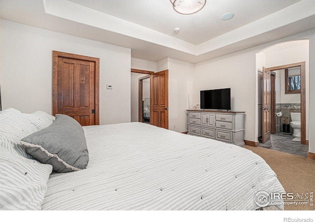 bedroom featuring arched walkways, carpet, a tray ceiling, and ensuite bathroom