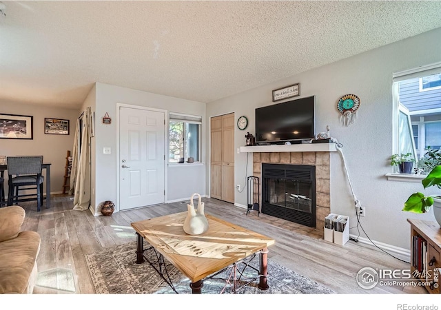 living room with a textured ceiling, a fireplace, baseboards, and wood finished floors