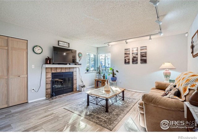 living area with light wood-style floors, a tiled fireplace, baseboards, and a textured ceiling