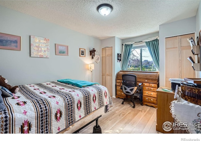 bedroom featuring a textured ceiling, light wood-type flooring, and two closets