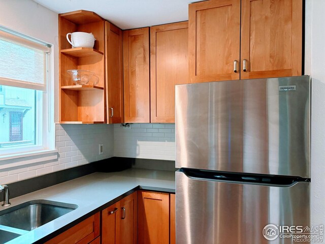 kitchen with open shelves, decorative backsplash, brown cabinets, freestanding refrigerator, and a sink