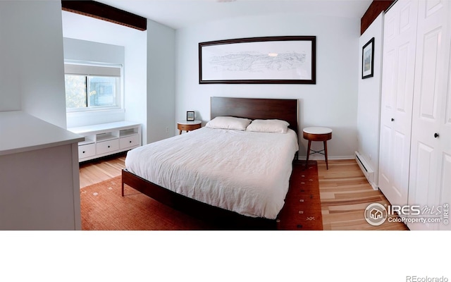 bedroom featuring a closet, baseboards, a baseboard heating unit, and light wood-style floors