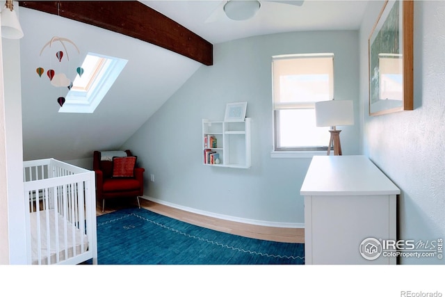 bedroom with vaulted ceiling with skylight, a crib, baseboards, and wood finished floors