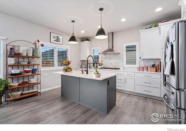 kitchen with light countertops, backsplash, appliances with stainless steel finishes, wall chimney range hood, and light wood-type flooring