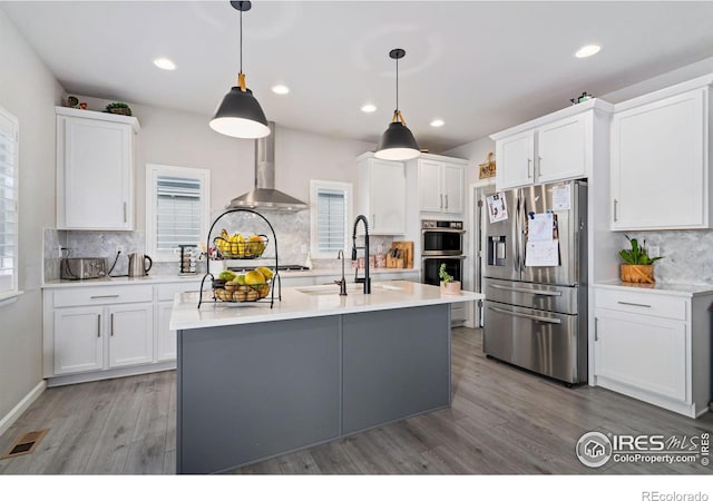 kitchen featuring stainless steel appliances, wall chimney range hood, light countertops, and visible vents