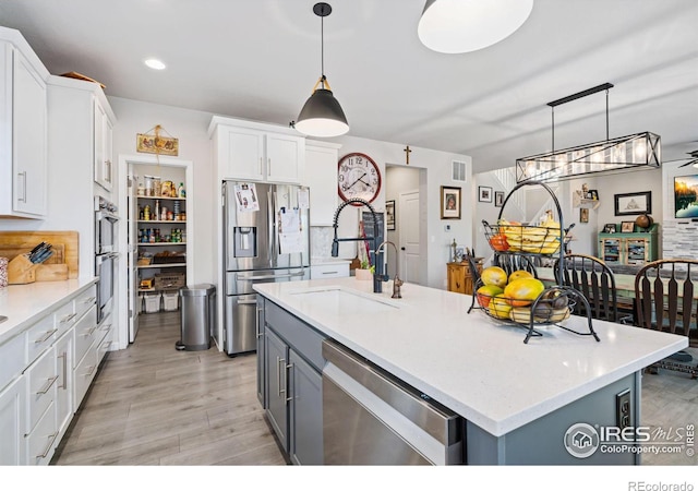 kitchen with white cabinets, appliances with stainless steel finishes, hanging light fixtures, light wood-type flooring, and a sink