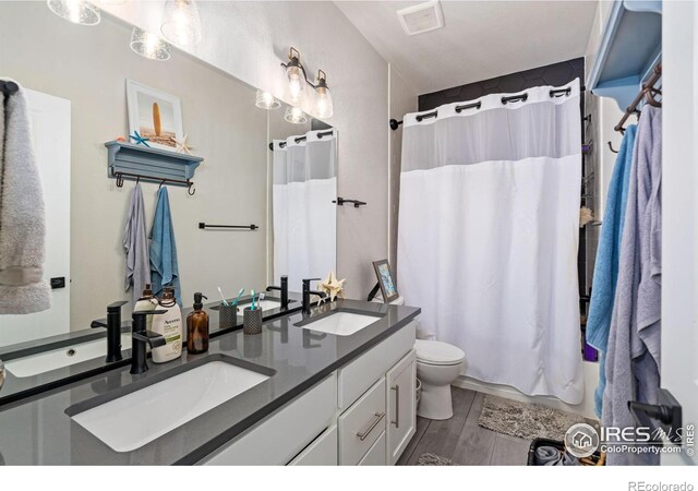 full bathroom featuring toilet, double vanity, a sink, and wood finished floors